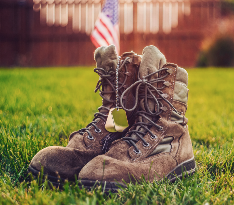 Military combat boots with dog tags on grass with American flag in background